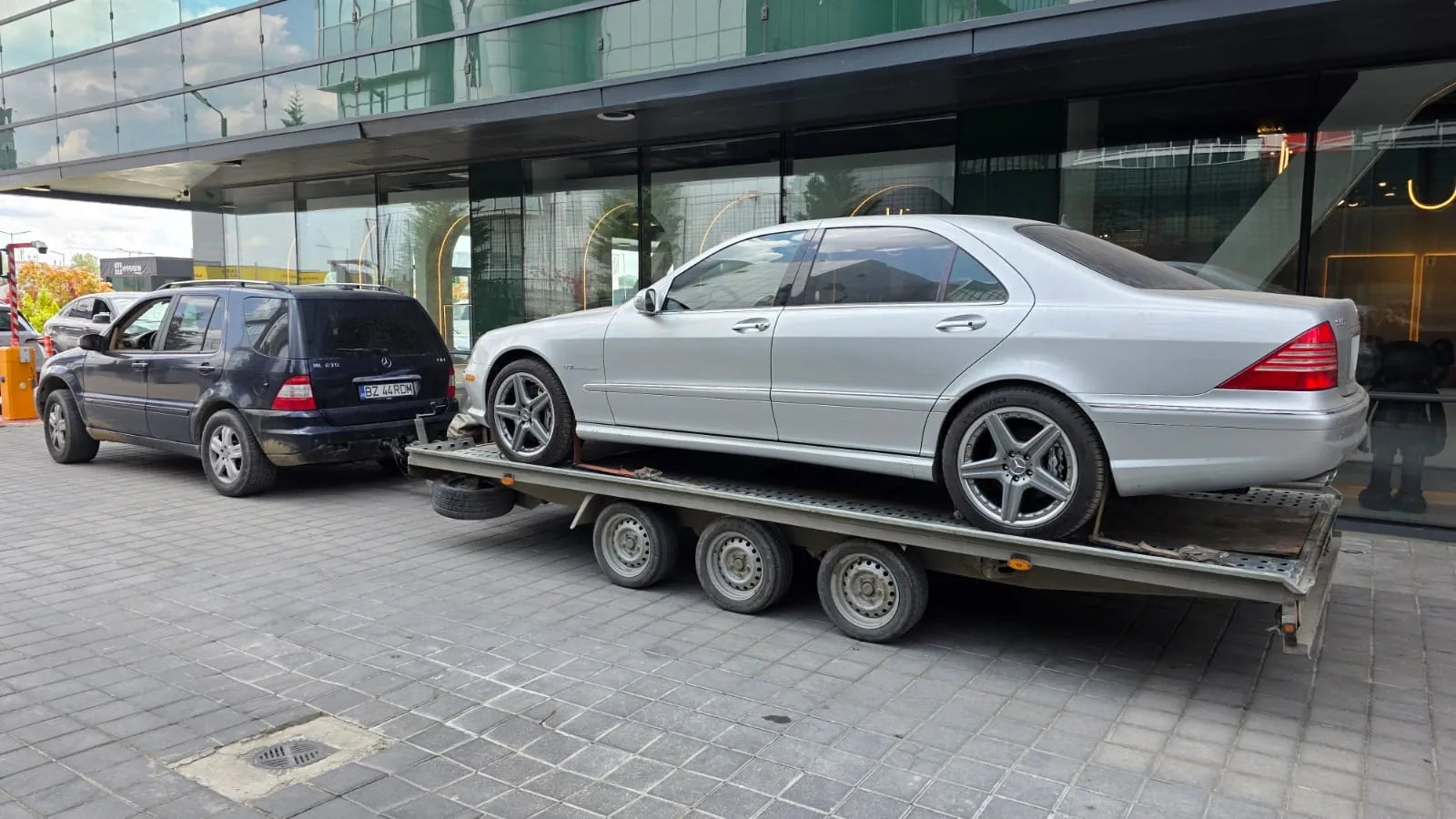 Mercedes ML care tractează o remorcă-platformă cu trei axe, încărcată cu un Mercedes Clasa S argintiu